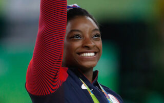 Simone Biles receiving her all-around gold medal at the Brazil 2016 Olympics. By Agência Brasil Fotografias - Crop of File:Simone Biles at the 2016 Olympics all-around gold medal podium (28262782114).jpg, CC BY 2.0, https://commons.wikimedia.org/w/index.php?curid=73989999