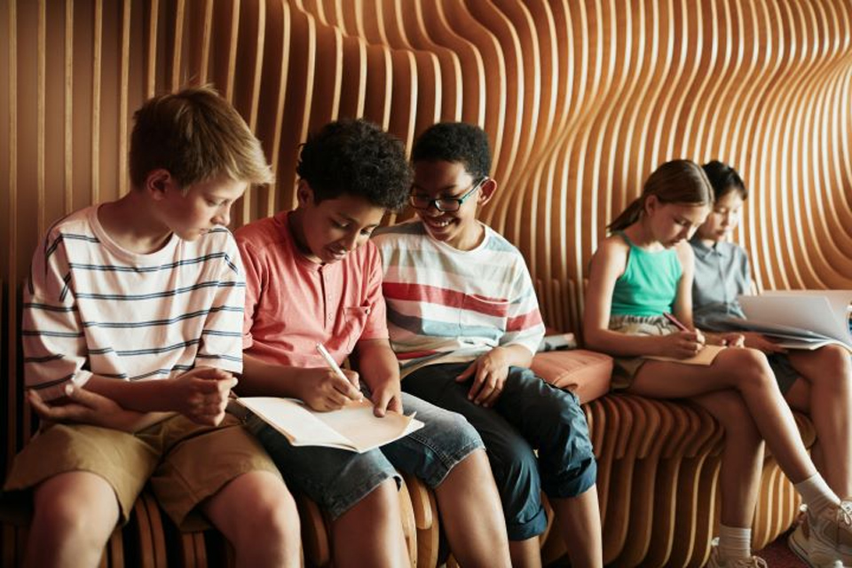 Children sitting on a wavybacked seat writing