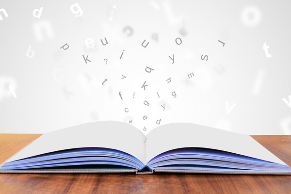 Open book on desk with letters magically springing out of the pages