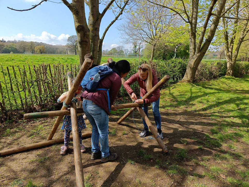 two women and a child building wooden tent poles together