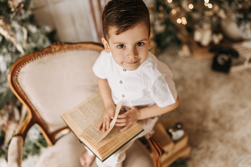 young child sitting reading a book near a Christmas tree