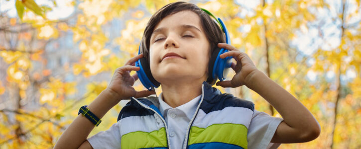 young boy with eyes closed and holding onto his headphones surrounded by beautiful autumn trees